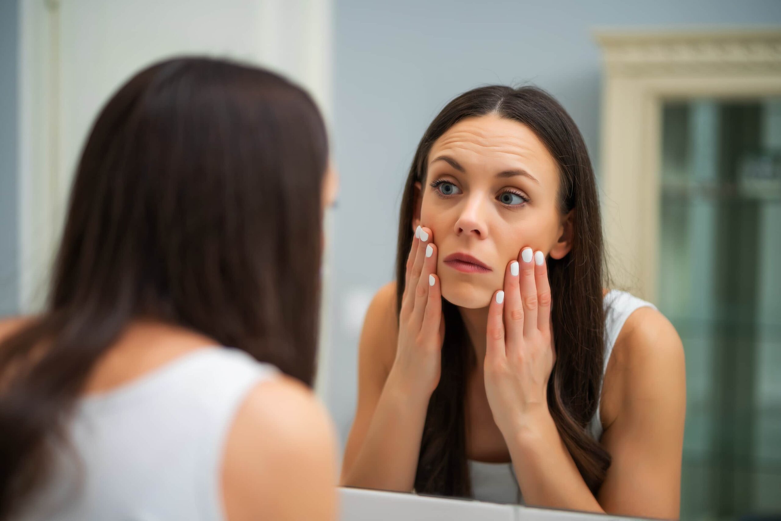 Woman with hands to face looking in mirror